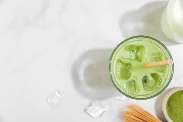 Matcha latte verde helado en un vaso sobre una superficie blanca con sombras duras