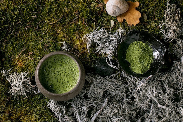 Matcha de té espumoso verde caliente tradicional japonés en taza de cerámica y matcha en polvo sobre musgo del bosque como fondo. Bebida natural saludable. Vista superior
