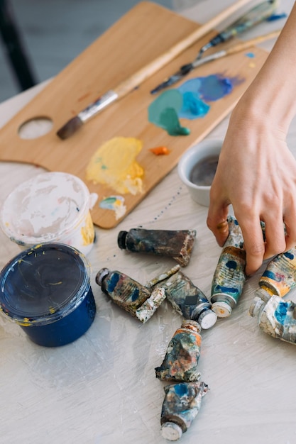 Materiais de pintura Aula de arte Passatempo criativo Artista feminina profissional escolhendo a mão o tubo de tinta acrílica ou a óleo no local de trabalho com ferramentas de paleta e pincel