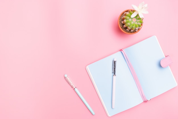 Material de escritório de mesa de trabalho com cacto em fundo rosa pastel