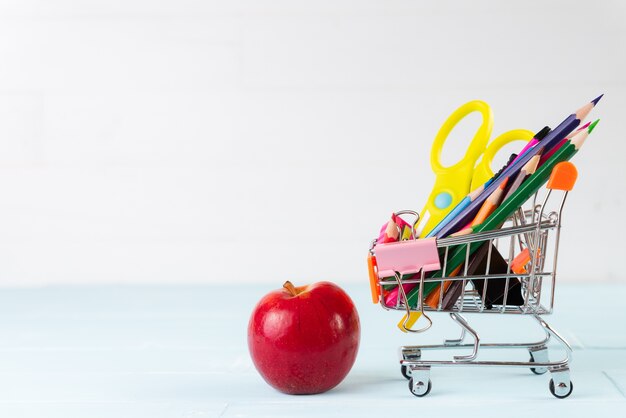 Material de escritório escolar com maçã vermelha, lápis no mini carrinho de compras.