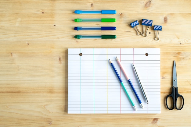 Material de escritório fixo na mesa de madeira - clipes, tesouras, papel de caderno em branco, lápis, caneta e marcadores de texto