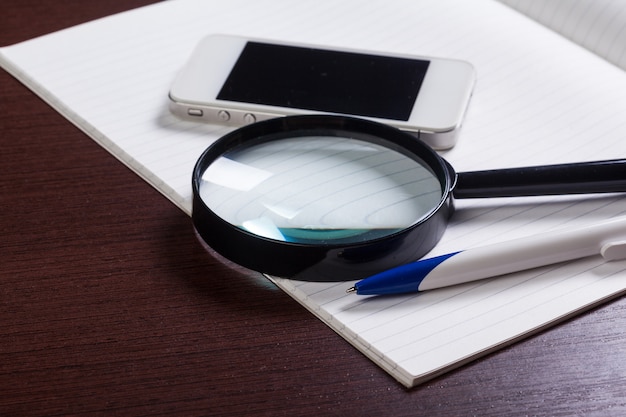 Foto material de escritório sortido com telefone celular e lupa na mesa de madeira