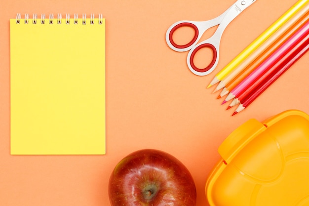 Material escolar. Caderno, apple, tesoura, lápis de cor e lancheira em fundo rosa. Vista superior com espaço de cópia. De volta ao conceito de escola. Cores pastel