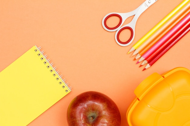 Material escolar. Caderno, apple, tesoura, lápis de cor e lancheira em fundo rosa.