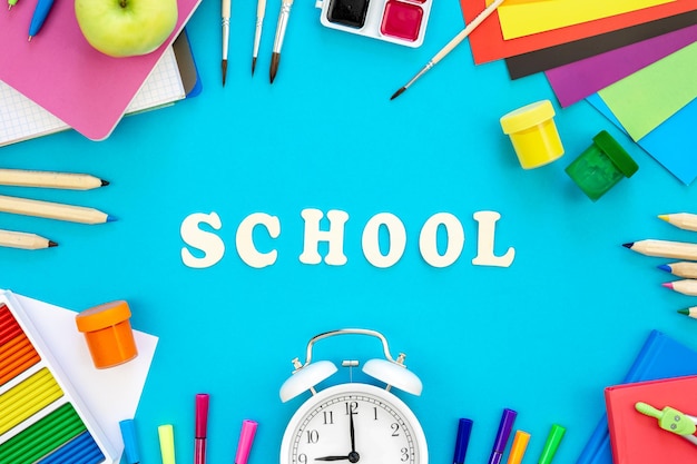 Material escolar colorido e letras de madeira em fundo azul de volta ao conceito da escola vista superior