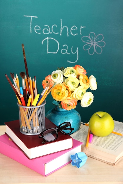 Material escolar e flores no fundo do quadro-negro com a inscrição teacher day