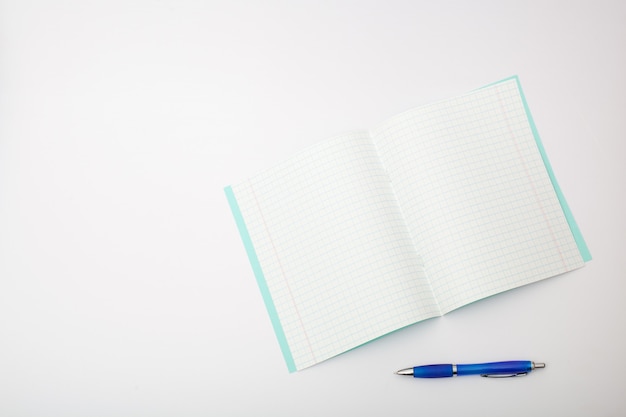 Material escolar isolado no fundo branco. foto sobre o tema dos estudos na escola. caderno e uma caneta esferográfica azul em um fundo branco