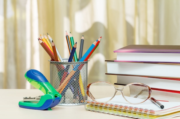 Material escolar. Livros, lápis de cor, óculos, caderno, caneta, grampeador na mesa de madeira Volta ao conceito de escola