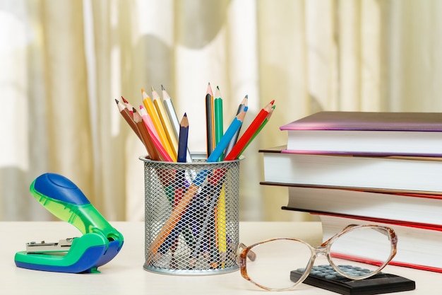 Material escolar. Livros, lápis de cor, óculos, calculadora, grampeador na mesa de madeira. Conceito de volta às aulas