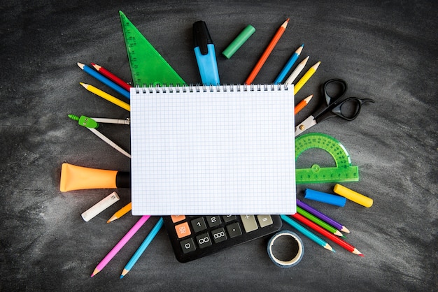 Material escolar no fundo do quadro negro. lápis de cor, calculadora, regras e cadernos. de volta ao conceito de escola.