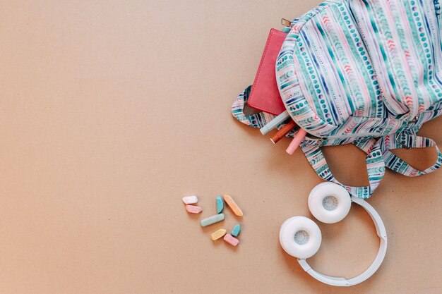 Material escolar plano yacía sobre fondo de papel artesanal. Mochila azul, auriculares blancos, cuaderno y bolígrafos con espacio de copia.