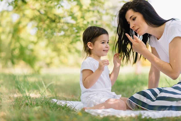 Maternidade e infância Linda mãe e sua linda filha cuidando e brincando ao ar livre na grama verde Linda mãe e seu filho alegre se divertem no parque juntos Retrato de família feliz