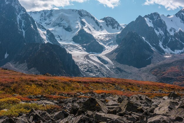 matorrales rojos en el paso iluminado por el sol con vistas a la gran cordillera de nieve con glaciares y cascadas de hielo en el día soleado de otoño colores vívidos de otoño en las altas montañas colina Motley y montañas nevadas en el sol brillante