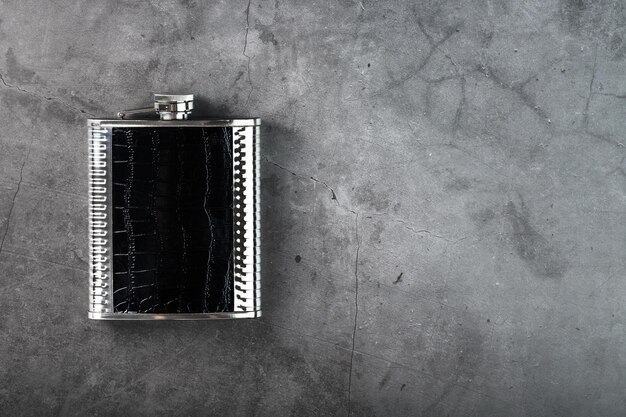 Matraz de bolsillo de acero con acabado de cuero con una bebida alcohólica sobre un fondo oscuro con espacio para copiar