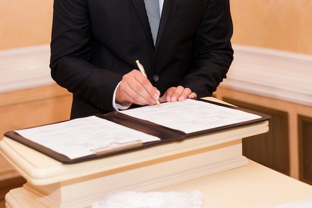 Matrimonio firmando registro, con pluma y documento oficial novios