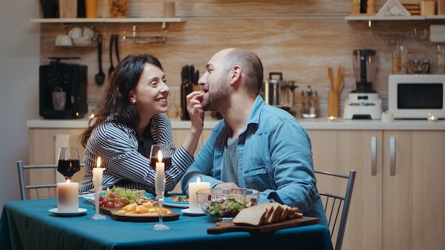 Matrimonio joven que tiene momentos divertidos en la cena. Esposa y esposo durante una cena romántica en la cocina, cenando juntos en casa, disfrutando de la comida, celebrando su aniversario, vacaciones sorpresa