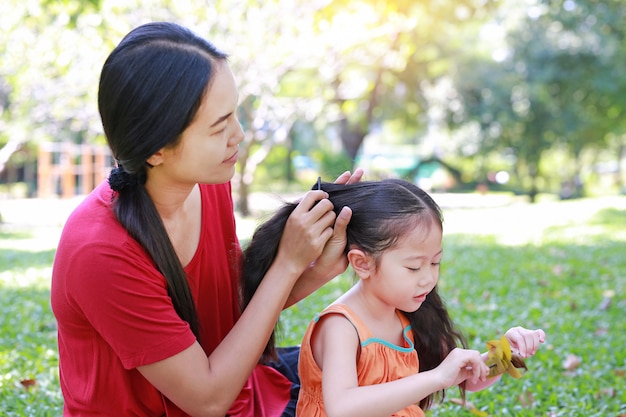 Matriz que penteia o cabelo da filha que encontra-se no jardim verde.