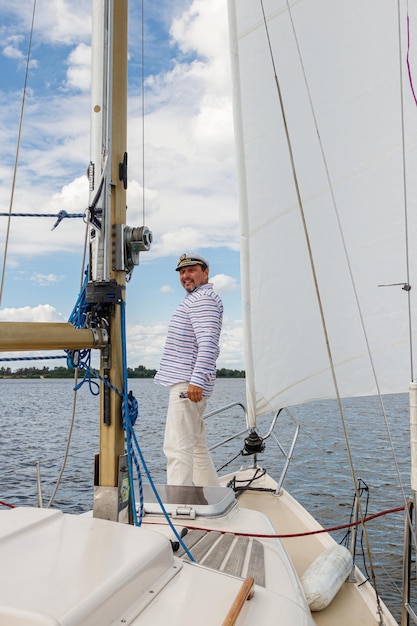 Matrosenmann in einer Kappe auf einem Boot unter Segeln gegen den Himmel und das Wasser