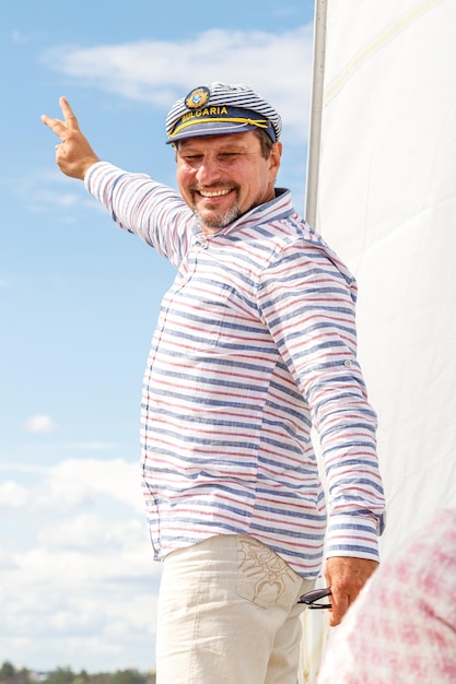 Foto matrosenmann in einer kappe auf einem boot unter segeln gegen den himmel und das wasser