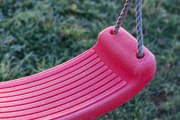 Foto mattierte kinderschaukel vor dem hintergrund von grünem gefrorenem gras selektiver fokus