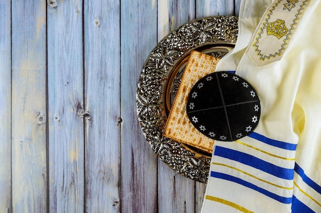 Foto matzoh pan de la pascua judía en el plato tradicional del seder con kipah y tallit sobre una mesa de madera
