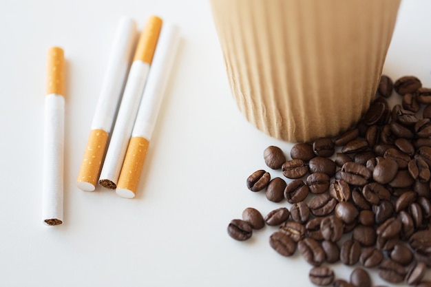 maus hábitos, vício e conceito de estilo de vida pouco saudável - close-up de cigarros, xícara de café e feijão na mesa