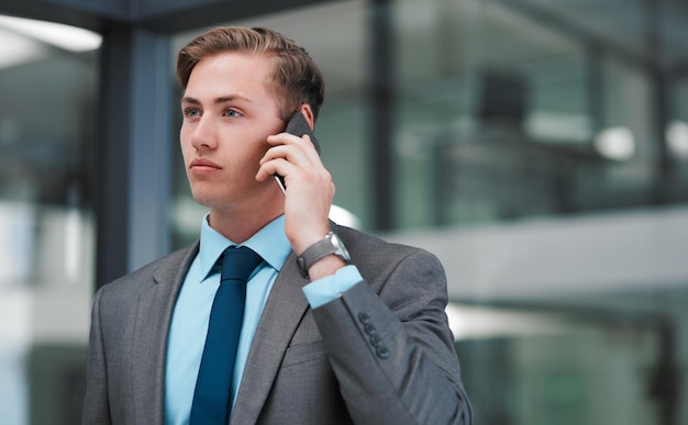 La mayor parte de mi negocio se hace por teléfono Captura recortada de un apuesto joven hombre de negocios parado solo en su oficina y usando su teléfono celular