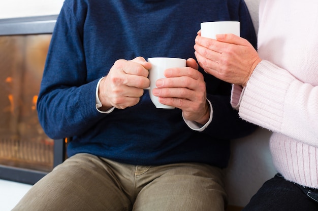 Mayores en casa frente a la chimenea con taza de té