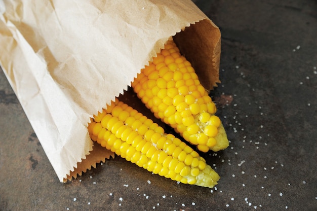 La mazorca de maíz dulce está en una bolsa de papel sobre la mesa con sal.
