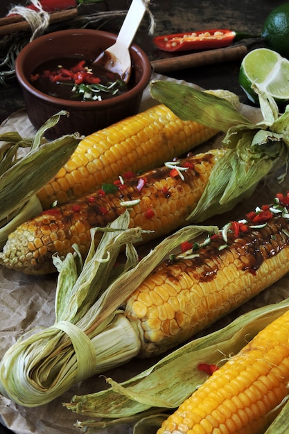 Mazorcas de maíz al horno en las hojas en una bandeja para hornear. Salsa de chile y lima.