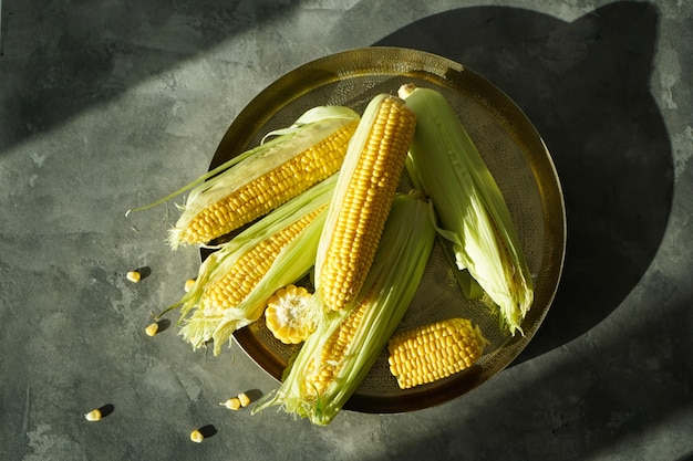 Mazorcas de maíz maduras en una bandeja de cobre sobre un fondo gris. Endecha plana.