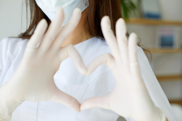 MD femenino en bata médica que muestra el símbolo del corazón por las palmas de pie aislado en el fondo de la oficina