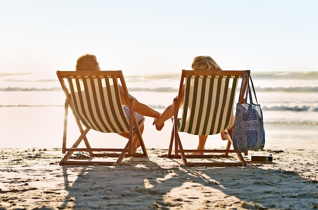 Me aferraré a ti para siempre Foto de una pareja tomados de la mano mientras observa la puesta de sol en una playa