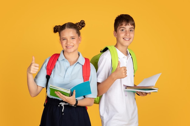 Foto me alegra que los niños y niñas adolescentes caucásicos inteligentes con mochilas de libros muestren sus pulgares hacia arriba