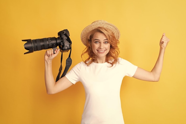 Me alegro de la exitosa fotógrafa pelirroja con cámara en sombrero de paja haciendo felicidad fotográfica