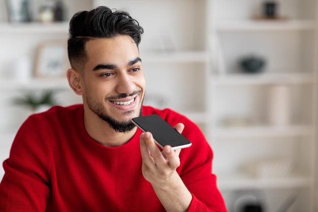 Me alegro de que un árabe milenario atractivo con barba vestido de rojo hable por teléfono en el lugar de trabajo en casa