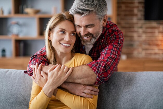 Me alegro de que un hombre europeo de mediana edad abrace a una mujer que disfrute de la comodidad y el romance en el sofá de la acogedora sala de estar