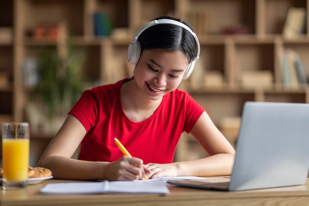 Me alegro de que una joven estudiante china con síndrome de down en los auriculares escuche una conferencia en línea y haga la tarea