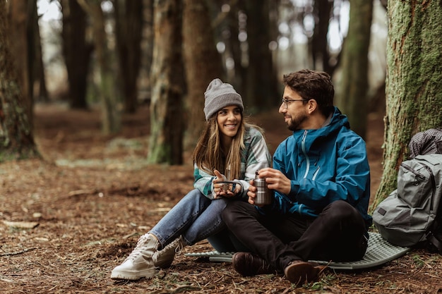 Me alegro de que los jóvenes europeos, hombres y mujeres, turistas en chaquetas con mochila descansen en un campamento forestal disfruten de la temporada fría