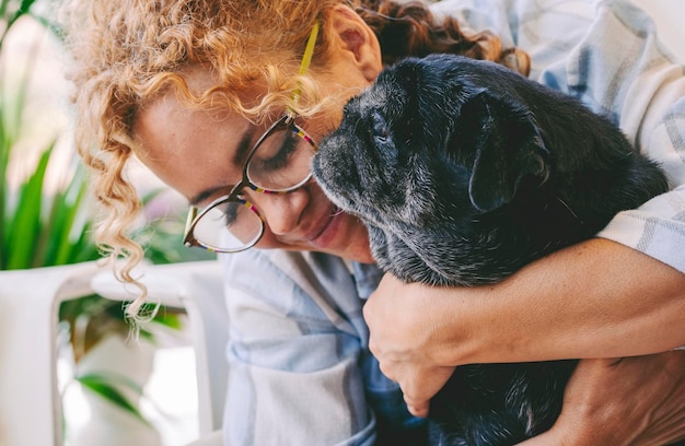 Me encanta la gente y el concepto de animal de perro con una mujer caucásica adulta feliz y un viejo pug negro abrazándose y amándose con ternura juntos. Concepto de mejores amigos para siempre