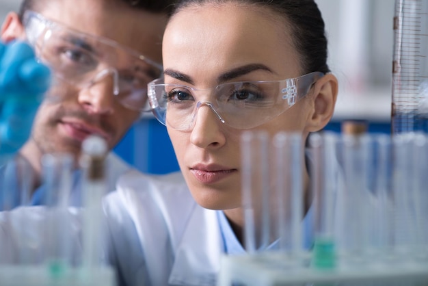Me encanta nuestro trabajo Dos científicos de perspectiva inteligente y responsable con gafas y guantes de goma que trabajan en el laboratorio manteniendo el vial y concentrándose en el proceso