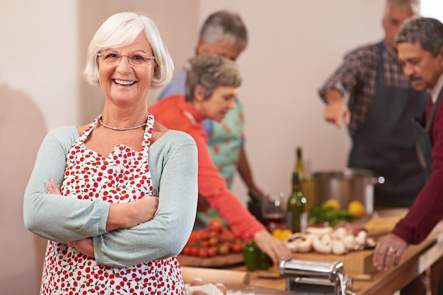 Me encanta organizar cenas Retrato de una mujer mayor con amigos cocinando juntos en el fondo