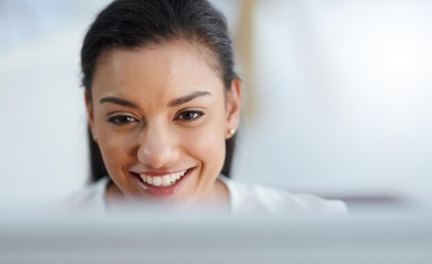 Me encanta este trabajo Foto de una alegre joven empresaria sonriendo y trabajando en su computadora en la oficina en el trabajo
