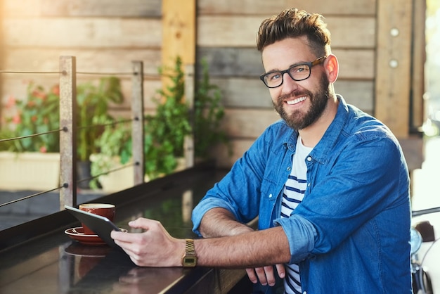 Me encanta venir aquí por el ambiente relajado Retrato de un joven apuesto que trabaja en una tableta digital en un café