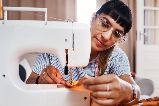 Me encanta ver a la gente en mis hermosas creaciones Captura recortada de una mujer joven cosiendo tela usando una máquina de coser en casa