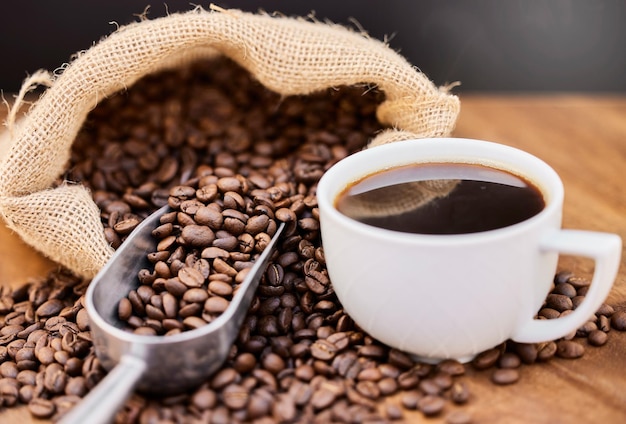 Me gusta mi café fresco y fuerte Toma de granos de café y una taza de café negro sobre una mesa de madera