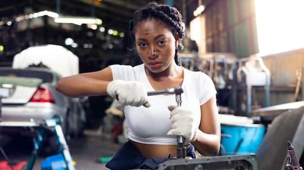 Mecánica de automóviles joven africana revisando y arreglando el motor del automóvil en el garaje de automóviles de servicio