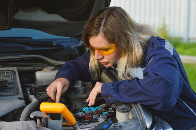 Una mecánica con gafas protectoras y overoles revisa los sistemas del automóvil en un espacio abierto