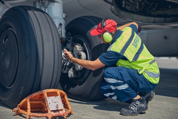 Mecánico de aeronaves calificado en ropa de trabajo que realiza una inspección visual del sistema del tren de aterrizaje del avión